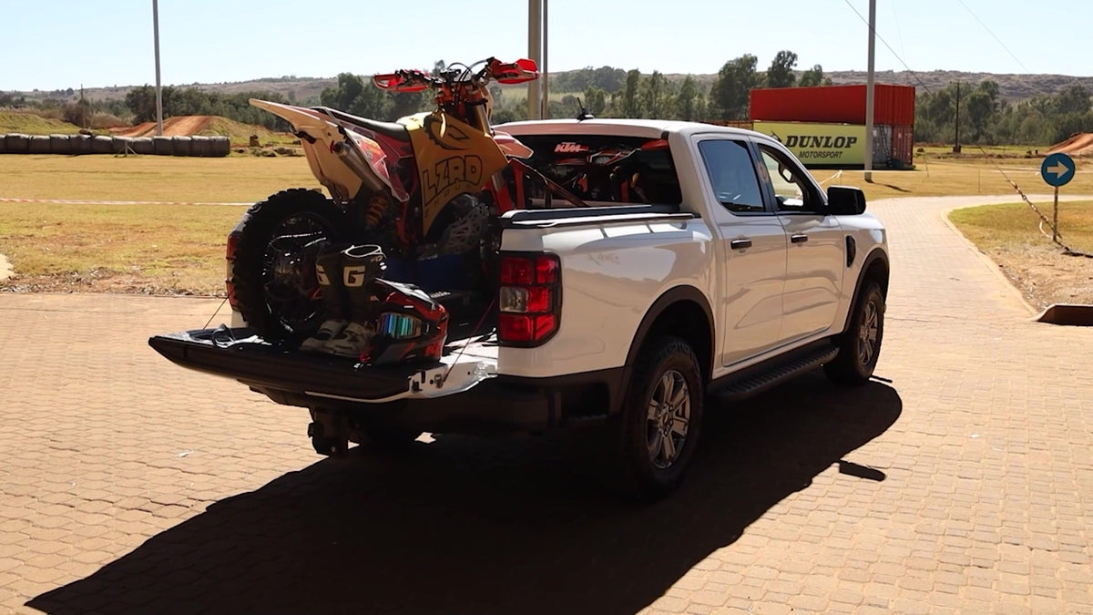 White Ford Ranger with a motocross bike in the open load bin at a motocross track.